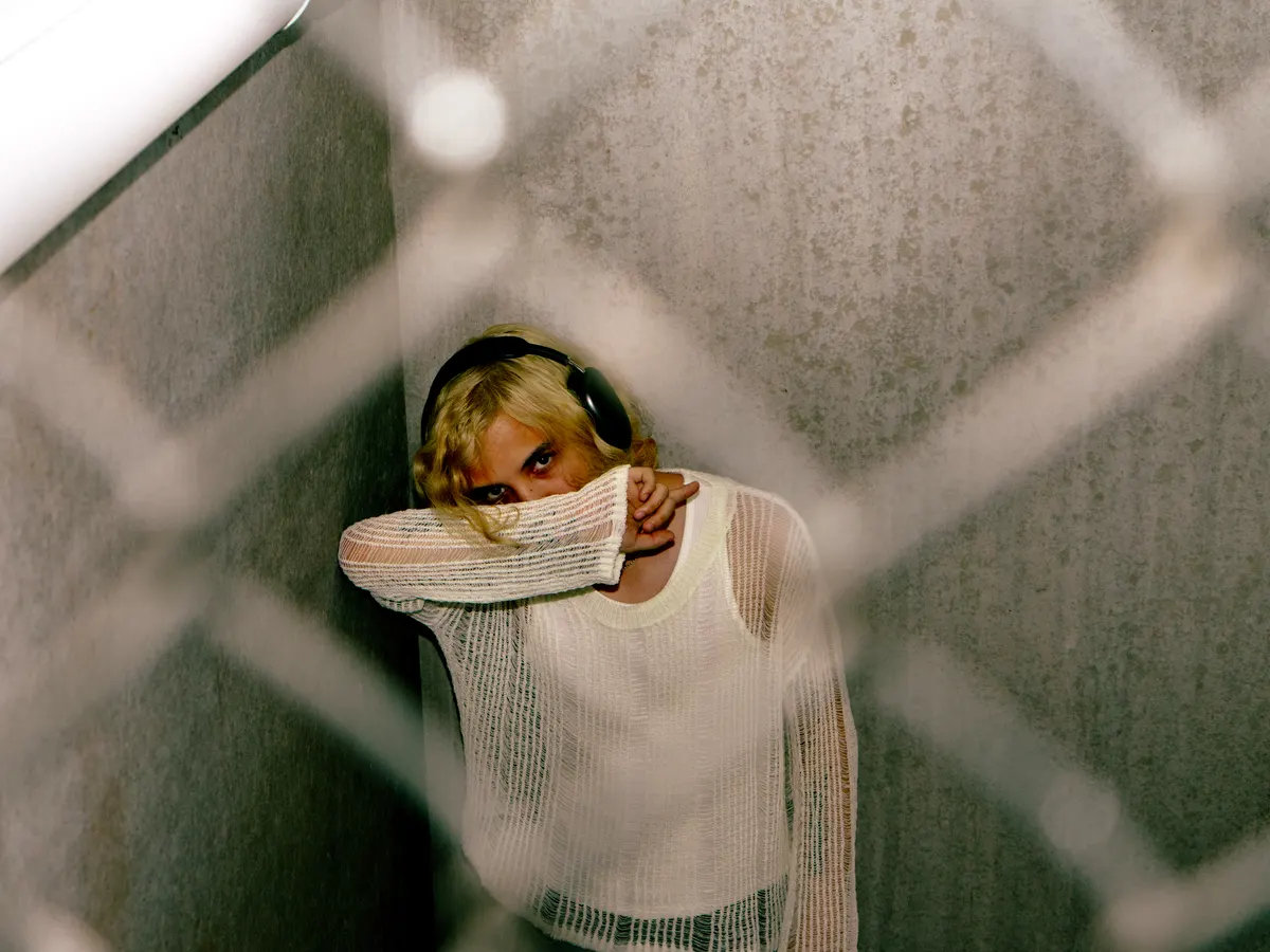 Jordan Andrew in headphones behind a chain-link fence